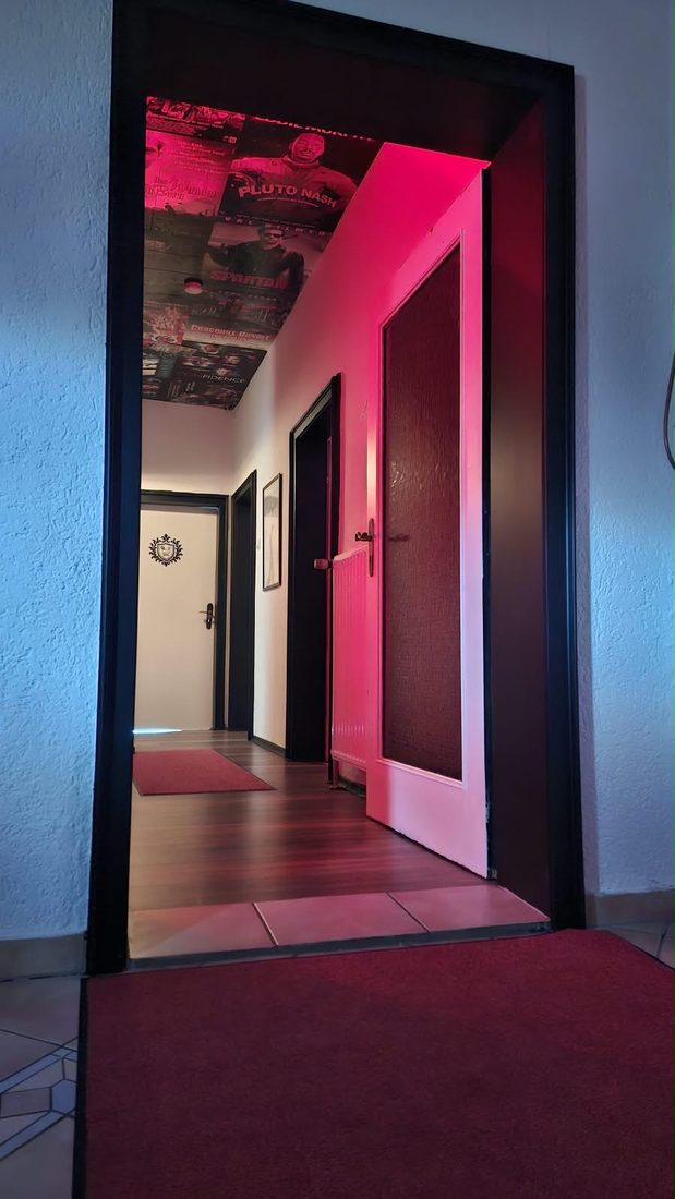 Offene Tür in den Flur mit roter Beleuchtung und Filmplakaten an der Decke